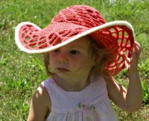 Menina em um jardim com chapéu de sol em crochê na cor goiaba