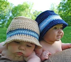 dois bebês usando chapéu de crochê. um na cor cru e outro a cor azul escuro, ambos com faixas azuis