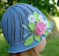 menina em jardim com chapéu azul claro com detalhe de uma rosa com folhagem