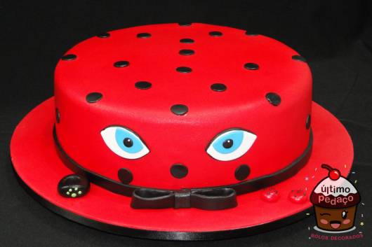 Bolo vermelho com bolas e laço preto e olhos azuis da Ladybug.