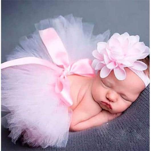 Bebê dormindo com saia rosa e acessório na cabeça.