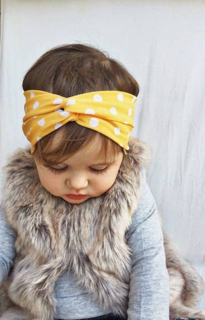 Bebe usa blusinha cinza e colinho de pele com turbante infantil estampado na cor amarelo e branco.