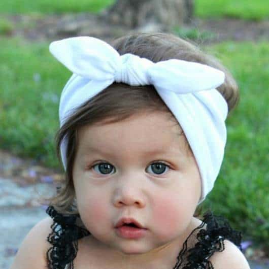 Bebê veste turbante branco ajustável com blusinha preta de alcinhas de renda.