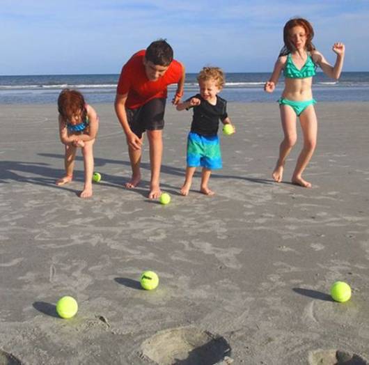 Crianças brincando com bolinhas de tênis na praia.