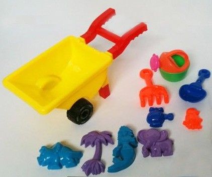 Carrinho de mão pequeno com formas, rastelo e outros brinquedos de praia.