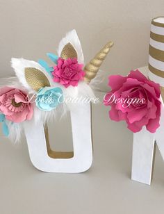 Letras decorativas brancas, com adereços em rosa, azul e dourado.