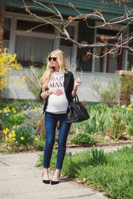 Modelo grávida veste, calça jeans azul, blusa básica branca,sapato, bolsa de mão e blazer preto.