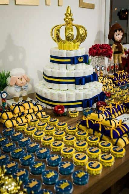 Mesa decorada com doces amarelos, azuis e bolo de fraldas.