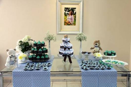 Mesa decorada com duas toalhas azuis, bolo de fraldas e ursinho.