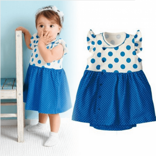 Bebê usa vestido azul com detalhes de bolinhas e tiarinha na mesma estampa.