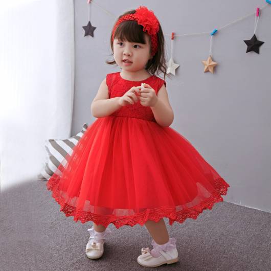 Bebê veste vestido vermelho alaranjado, com sapatinho branco e tiara vermelha.
