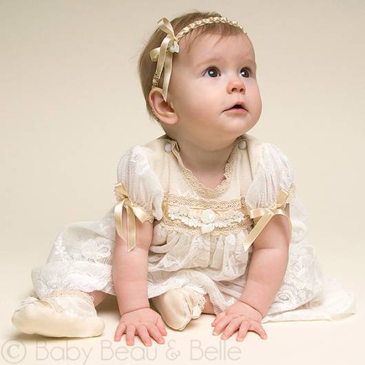 Bebê usa vestido com detalhes em amarelo de fitinhas decoradas, modelo de mangas bufantes.