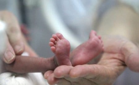Mãe segurando os pés de um bebê que nasceu de parto prematuro.