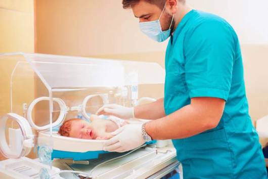 Médico segurando bebê na incubadora.